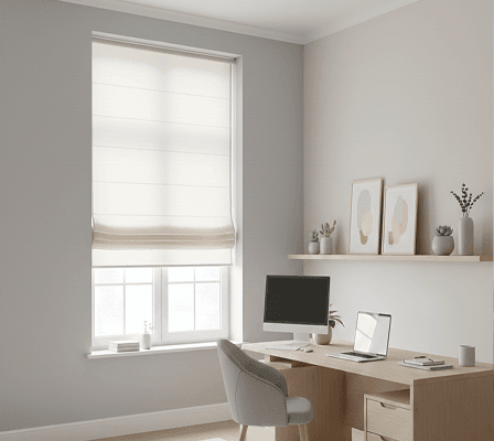 Minimalist home office with a light wooden desk, computer, and a window with Roman blinds.